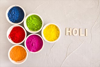 Holi text near different type color powder concrete background