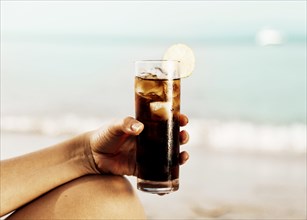 Glass coke with ice hand beach