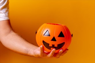 Hand holding an orange Halloween pumpkin on a yellow background