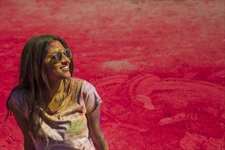 Portrait smiling young woman wearing sunglasses messing holi color