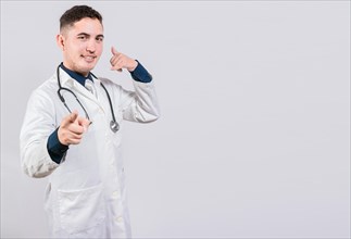 Handsome doctor making call gesture isolated. Smiling doctor making call gesture and pointing at the camera