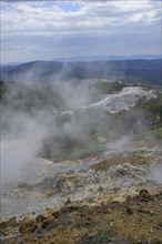 Steam rises above the colourful rubble deposits of the Biancane Geothermal Park and the town in the background