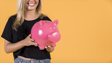 Smiling woman holding pink piggy bank against bright backdrop