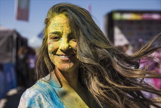 Smiling young woman covered her face with holi color looking camera