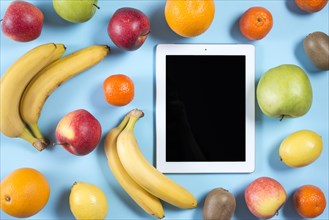 Blank digital tablet surrounded with whole healthy fruits blue background