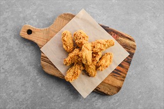 Top view of deep fried chicken wings in breading on wooden serving board
