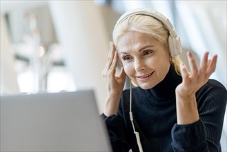 Elder business woman having video call laptop with headphones