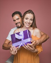 Beautiful couple holding purple gift box against colored background