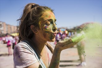 Close up young woman blowing holi color