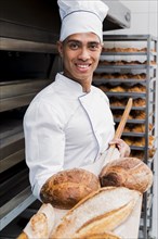 Portrait smiling young male baker showing freshly baked bread wooden shovel