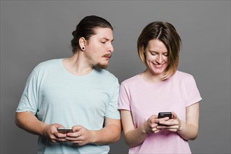 Young man spying peeking smartphone her girlfriend using mobile phone