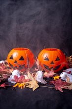 Halloween pumpkins over red autumn leaves and ghosts with smoke on a black background