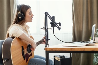 Female musician recording song home while playing acoustic guitar