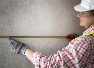 Side view female construction worker with helmet tape measurer