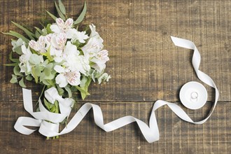 White ribbon flower bouquet with wedding rings plate wooden desk