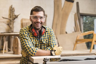 Smiling male carpenter with ear defender around her neck standing his workshop