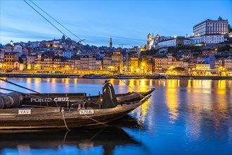 View over the traditional Rabelo boats on the Douro riverbank in Vila Nova de Gaia towards the old town of Porto at dusk