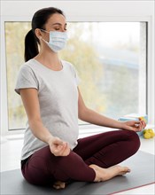 Pregnant woman with medical mask doing yoga