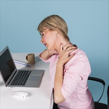 Woman sitting chair suffering from neck pain while using laptop