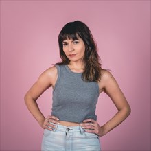 Studio portrait of a confidence woman with hands on hips while looking at camera over a pink background