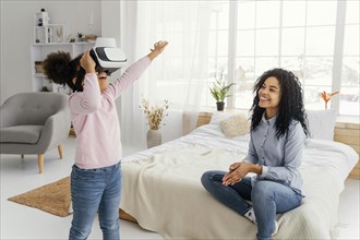 Smiley mother watching daughter play with virtual reality headset