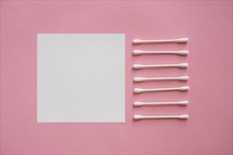 Row cotton swabs near blank adhesive note pink background