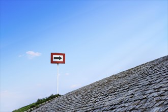 Black arrow on white background and in red frame standing atop of cobblestone paved hill at day. Blue sky with great clouds. Copy space