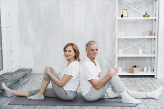 Happy senior couple sitting back back grey yoga mat