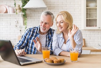 Senior couple waving their hands during online video call laptop