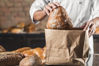 Male baker putting baked bread brown paper bag