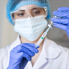 Female researcher with safety glasses medical mask holding syringe