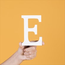 Close up hand holding up uppercase capital letter e yellow background