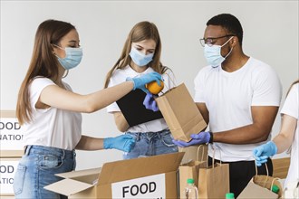 Volunteers with gloves medical masks preparing box with food donation