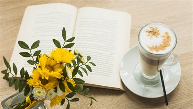 Flower vas latte coffee cup with open book wooden textured surface