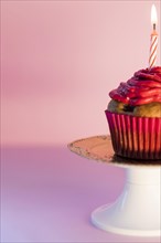 Close up lighted candle cupcake cakestand against pink background