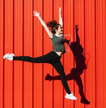 Lovely woman leaping near red wall