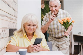 Elderly man preparing surprise with bouquet wife