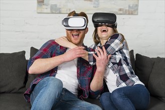 Excited young couple sitting sofa using vr headset experiencing virtual reality