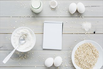 High angle view spiral notepad oats eggs flour milk wooden backdrop