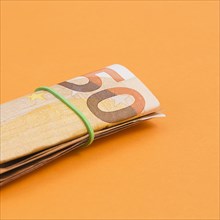 Close up rolled up euro note tied with rubber orange backdrop
