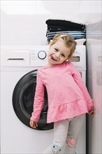 Portrait cute girl standing front washing machine