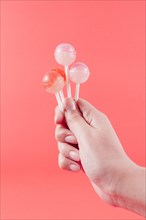 Close up woman s hand holding lollipops against coral backdrop
