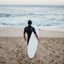 Man wearing surfer clothes walking sand from