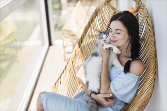 Young woman sitting chair patio loving her pet cat