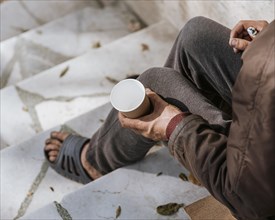 Homeless man holding empty cup stairs