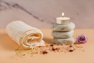 Rolled up towel lighted candle spa stones rose himalayan salts peach colored backdrop
