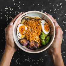 Woman s hand holding bowl noodles with eggs onion broccoli bowl black background
