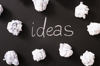 Ideas word surrounded with white crumpled paper balls blackboard