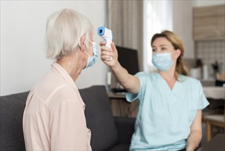 Female nurse checking elder woman s temperature