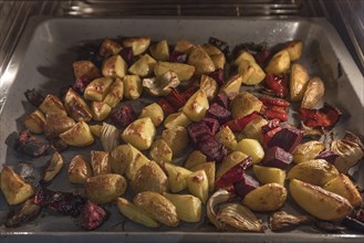 Vegetables and jacket potatoes on a baking tray in the oven